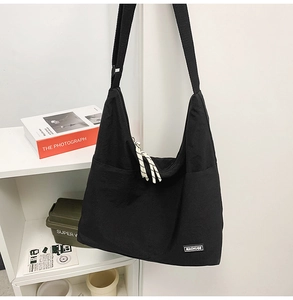 Detail of black canvas crossbody bag featuring wide strap and woven rope zipper pull