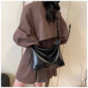 Model wearing large black hobo shoulder bag in glossy leather with fashion plate detail