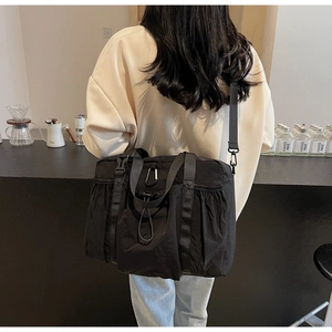 Detail of black nylon tote bag featuring adjustable shoulder straps and utility carabiner
