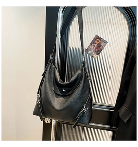 Detail of black lychee grain leather tote bag showing side metal buckle and drape texture