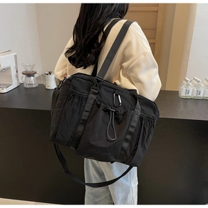 Detail of a black nylon bucket bag featuring side drawstring pockets and wide strap