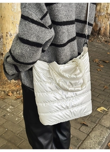 Outdoor shot of a white quilted tote bag worn crossbody with glossy down jacket material