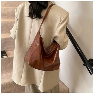 Close-up of brown oiled leather hobo bag worn by model in beige suit for daily commute