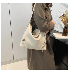 Detail of cream tote bag with metallic buckle adjustment worn with olive trench coat