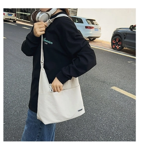 Outdoor shot of an off-white canvas crossbody bag with a wide front pocket and strap