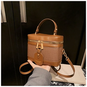 Close-up of brown leather and canvas bucket bag with gold zippers and brand tag