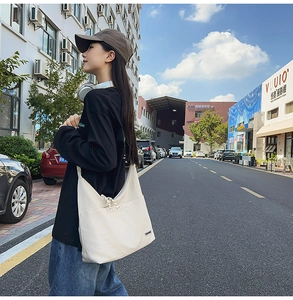 Close-up of cream canvas hobo bag with zip detail and woven label in street setting