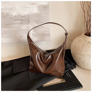 Close-up of a dark brown glossy leather hobo bag on a black blazer with artistic decor