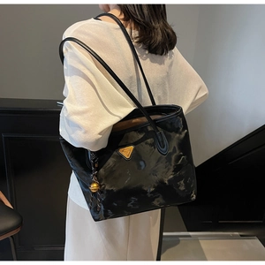 Schulteransicht einer schwarzen glänzenden Tragetasche mit Metalllogo und goldenem Anhänger