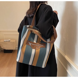 Detail of canvas striped tote bag featuring brown leather zipper pocket and metal rivets