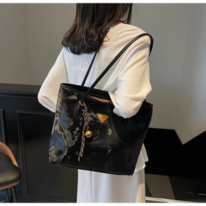 Detail der schwarzen glänzenden Falten-Tote-Bag mit Metalldreieck und Anhänger
