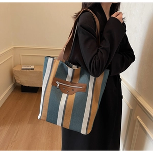 Detail of canvas striped tote bag featuring brown leather pocket and vintage metal rivets