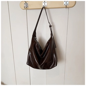 Detail of dark brown glossy PU leather hobo bag with adjustable strap on wooden hanger