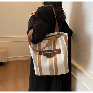 Detail of striped canvas tote bag showing wide brown strap and leather zipper patch