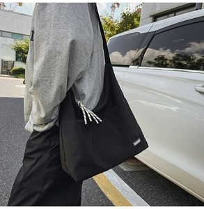 Detailed macro view of minimalist black shoulder bag with MACHUYI woven label and rope zipper pull