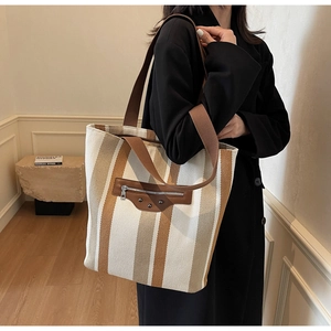 Close-up of a striped canvas tote bag with leather zipper detail and studded accents