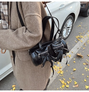 Détail d'un sac cylindre en cuir verni noir avec nœuds en soie sur un manteau brun