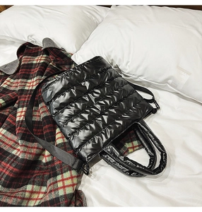 Detail of black quilted puffer tote bag with glossy finish and detachable shoulder strap