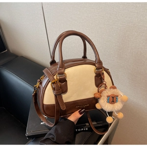 Detail of two-tone crossbody bag with plush charm on a leather sofa background