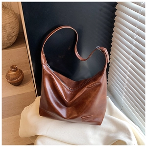 Detail of the high-shine oily leather texture and fashion label on the brown crossbody bag