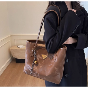 Detail einer braunen Tote-Bag mit Marmormuster, goldenem Dreieckslogo und Anhänger