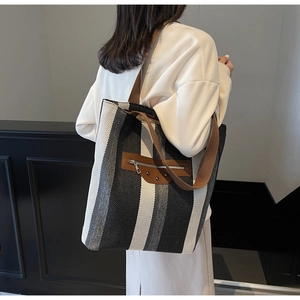 Detail of striped woven tote bag with brown leather patch and metal studs on shoulder