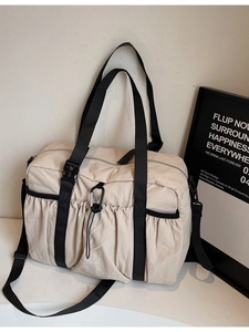 Minimalist beige travel duffel bag with black straps and a front pleated pocket