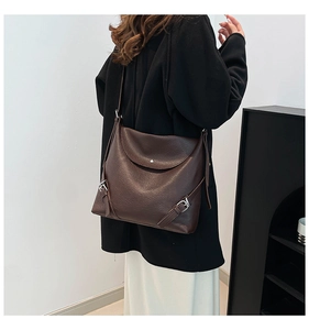 Detail of dark brown lychee leather texture and silver hardware on a crossbody tote bag