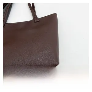 Detailed close-up of stitching and textured lychee pattern on dark brown leather tote bag