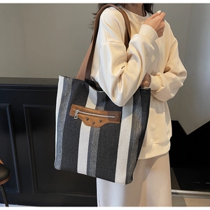 Detail view of large canvas tote bag featuring vertical stripes and brown leather zip pocket