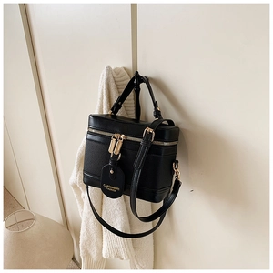 Detail of black box bucket bag featuring gold hardware and dual zippers on white backdrop