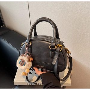 Detail of black shell bag with bronze hardware and a cute plush animal pendant