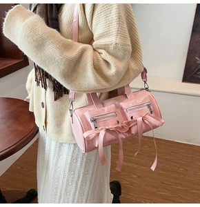 Sac cylindre rose en cuir verni avec nœuds porté par un mannequin dans un décor intérieur