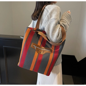 Detail of striped canvas tote bag featuring front leather zip pocket and metal studs