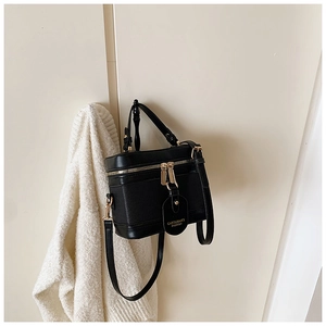 Detail of black box-shaped crossbody bag with gold zipper and textured synthetic leather