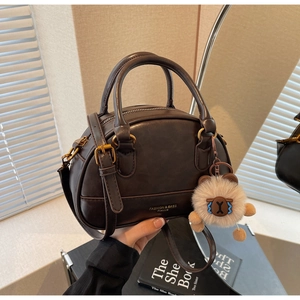 Detail of dark brown leather shell bag with gold hardware and plush bear charm