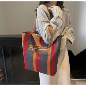 Close-up of striped canvas tote bag featuring brown leather pocket and metal rivets