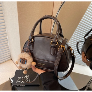 Detail of dark brown leather shell bag with gold lettering and lion plush keychain charm