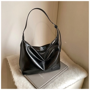 Close-up of black glossy leather shoulder bag with metallic zipper and adjustable strap