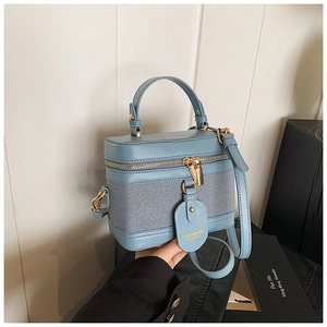 Detail of blue box-shaped handbag featuring textured fabric and gold zipper hardware
