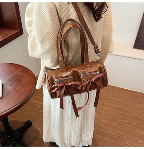 Détail du sac cylindrique marron avec des nœuds décoratifs et des poches à fermeture