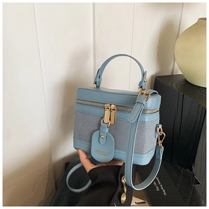Detail of blue vanity bag featuring fabric stitching, leather trim, and dual zippers