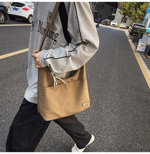 Detail showing the khaki nylon crossbody bag's front double pockets and woven zipper pull