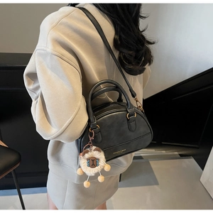 Detail of retro black matte shell bag with dual handles and cute white sheep pendant