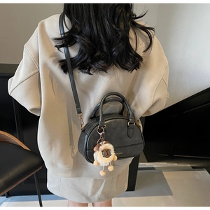 Detail of black faux leather shell bag featuring a cute white plush lamb pendant
