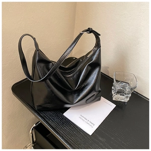 Detail of glossy black PU leather texture with silver zipper and brand tag on dumpling bag