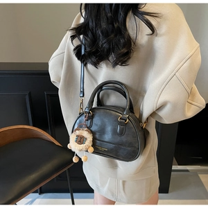 Detailed view of black shell bag featuring golden text print and a khaki teddy charm