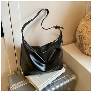 Close-up of a glossy black hobo bag with adjustable strap on a metallic suitcase