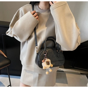 Detailed view of a black leather shell bag with a cute plush sheep pendant charm