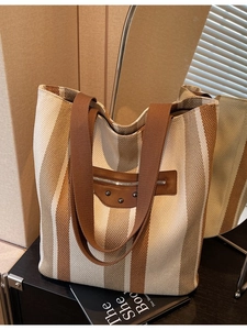 Vertical striped canvas tote bag with brown straps and rivet details in a home setting